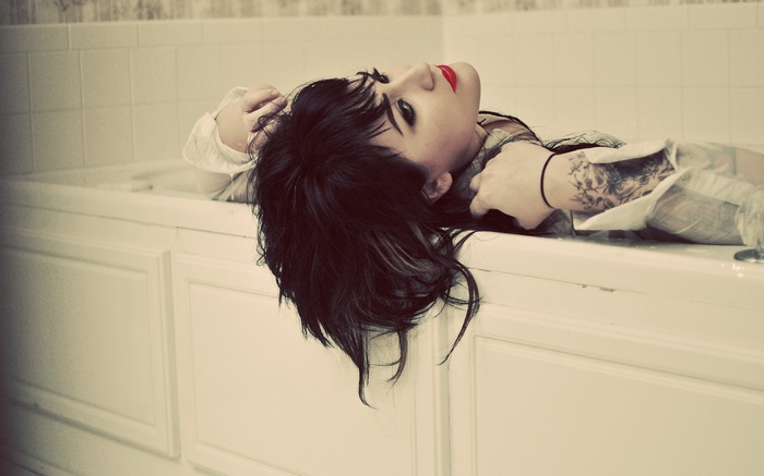 Woman with tattoo and red lipstick lying in a bathtub