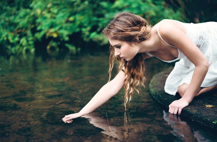 Woman in white dress touching water in a pond