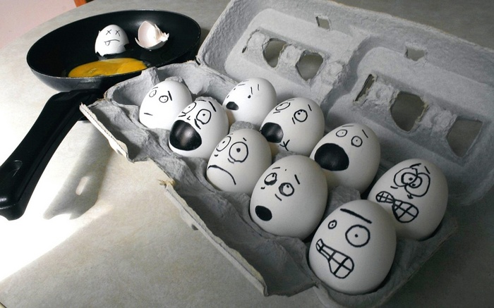 Eggs with drawn faces in a carton and a frying pan