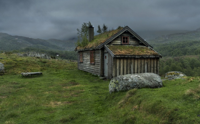 Wooden hut with grass roof in misty mountains