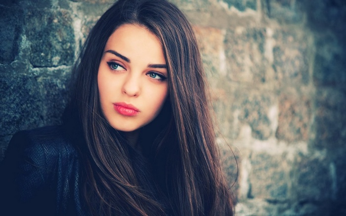 Woman with long hair leaning against a stone wall