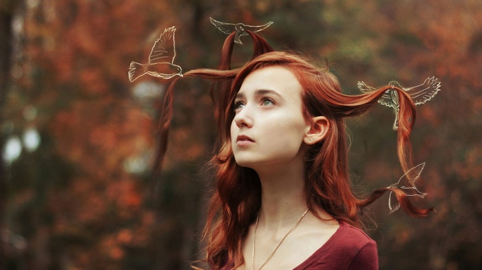 Redhead woman with birds in her hair in a forest
