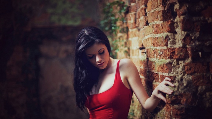 Woman in red tank top leaning against brick wall
