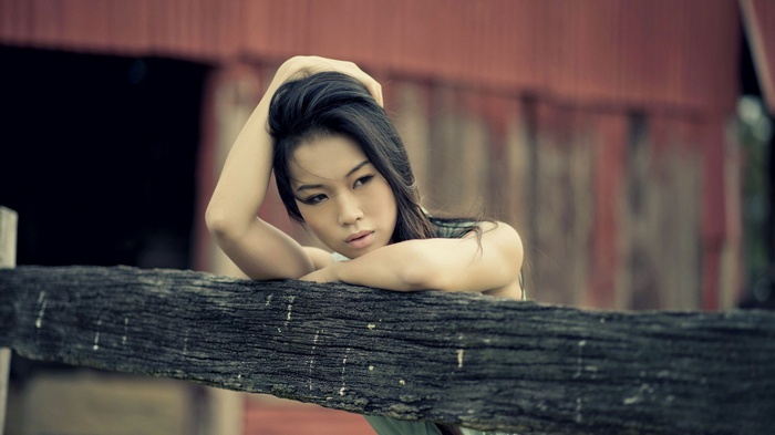 Asian woman leaning on a wooden fence outdoors