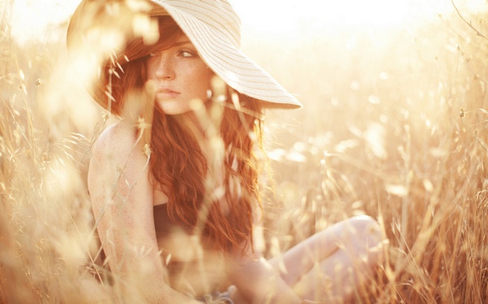 Redhead woman with freckles wearing a hat in a field