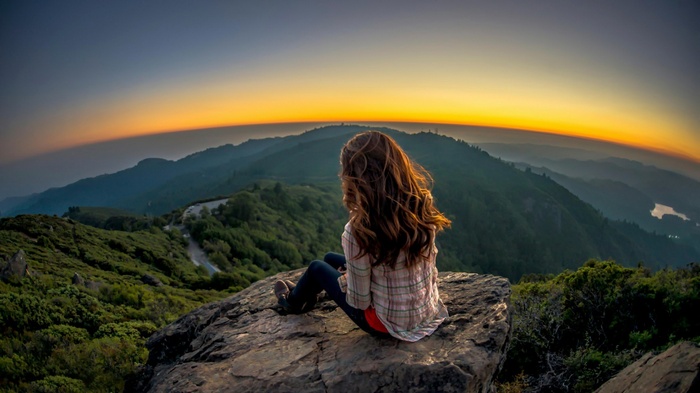 Woman sitting on a rock overlooking mountains at sunset