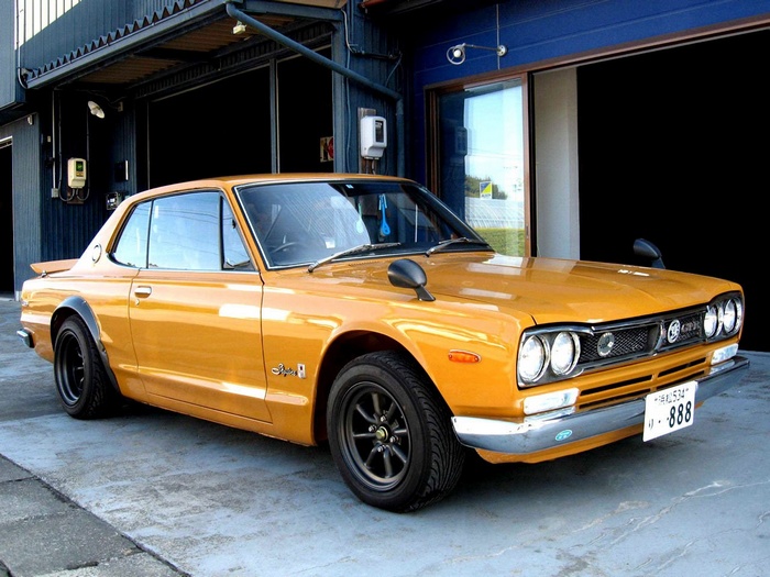 Orange Nissan Skyline 2000GT parked in front of a building
