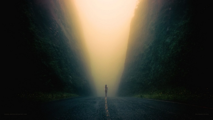Person walking on a road between mountains in fog