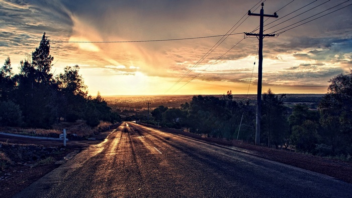Sunset over a wet road with trees and power lines