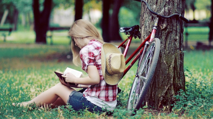 Woman reading a book next to a bicycle and tree