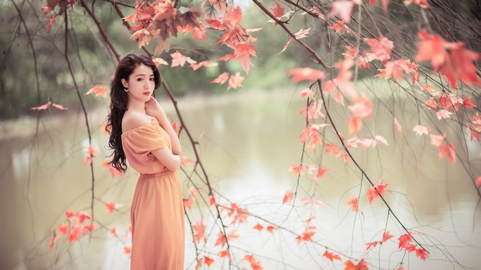 Woman in orange dress by a lake with fall leaves