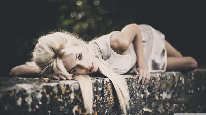 Blonde woman lying on a stone wall outdoors