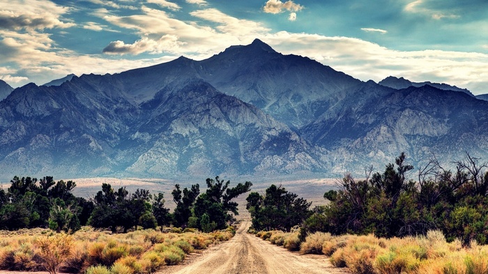 Dirt road leading to majestic mountains under a cloudy sky