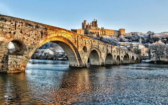 Stone bridge over a river with a castle on a snowy hill