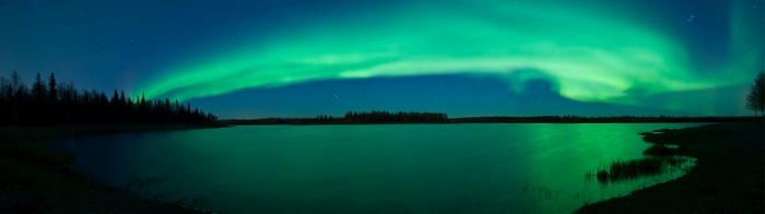 Aurora Borealis over a calm lake with trees