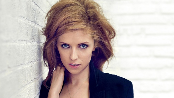 Anna Kendrick leans against a white brick wall