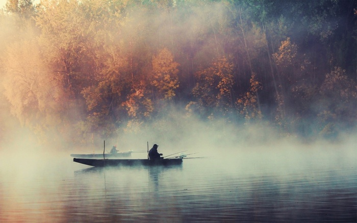 Fishermen in boats on a misty lake in autumn