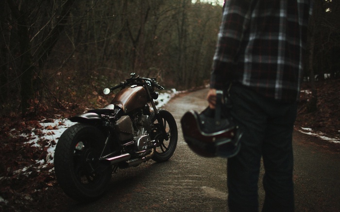 Man holding helmet next to a motorcycle on a road