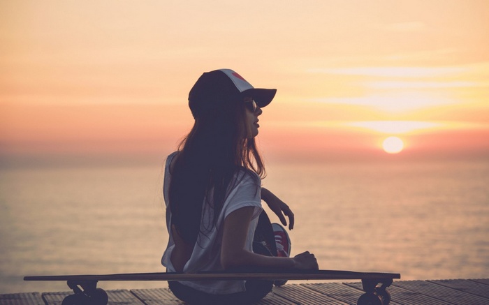 Woman with skateboard watching the sunset