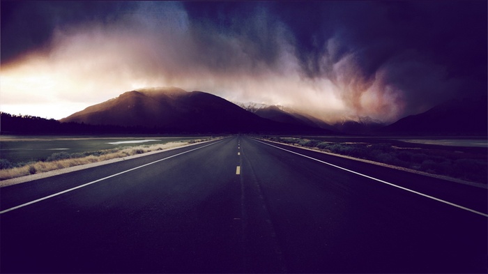 Road leading to mountains under stormy sky