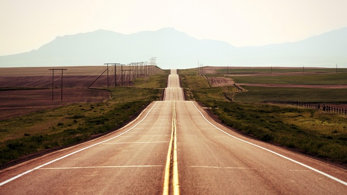 A long, empty highway stretches towards distant mountains.