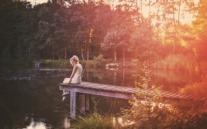 Woman sitting on a wooden pier by a lake