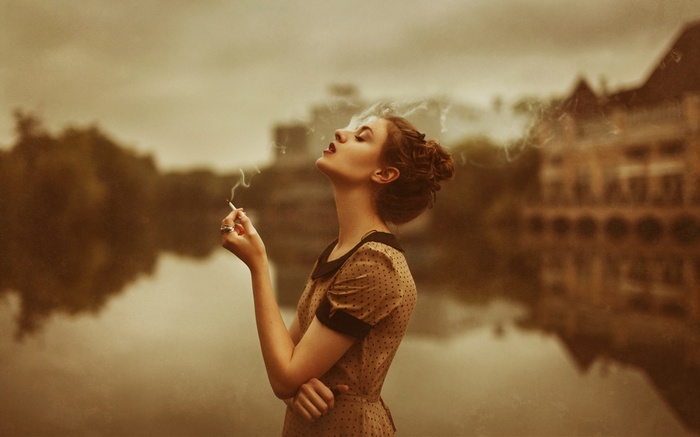 Woman smoking a cigarette outdoors by a lake