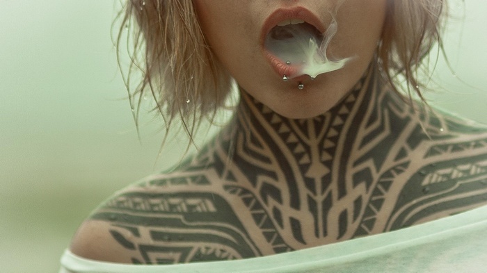 Teya Salat with piercings and tattoos exhales smoke