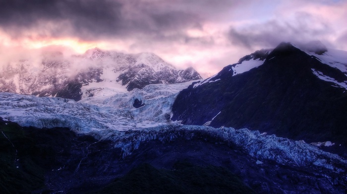 Glacier and snow-capped mountains in Alaska under dramatic clouds