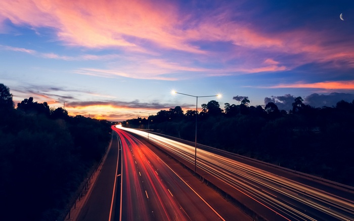 Highway light trails at sunset with a crescent moon