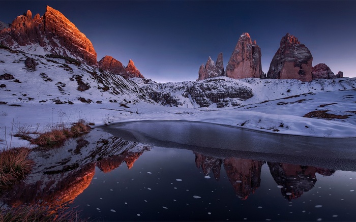 Snowy mountains reflected in a frozen lake at sunset