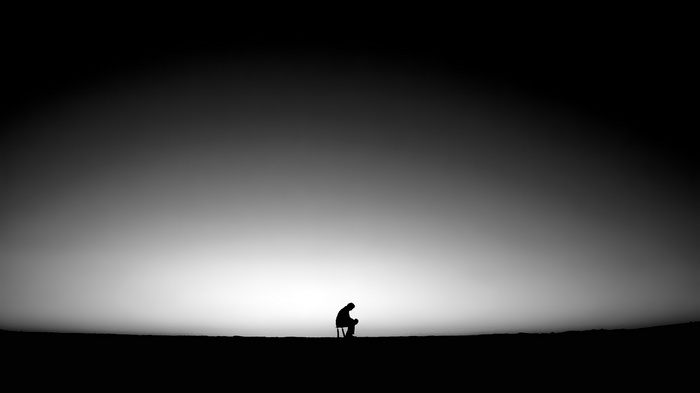 A lone figure sits in silhouette against a bright sky.