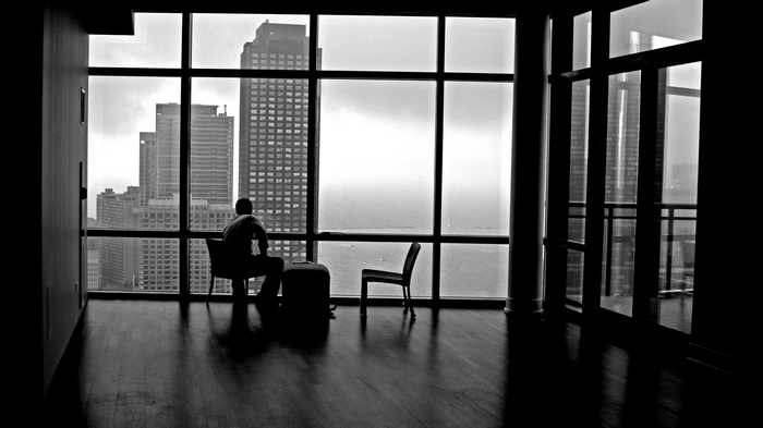 Man sitting by a large window overlooking a cityscape