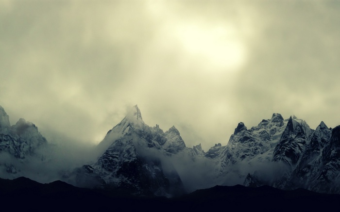 Snow-capped mountains shrouded in clouds under a bright sky