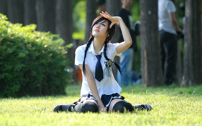 Asian woman in school uniform kneeling in grass