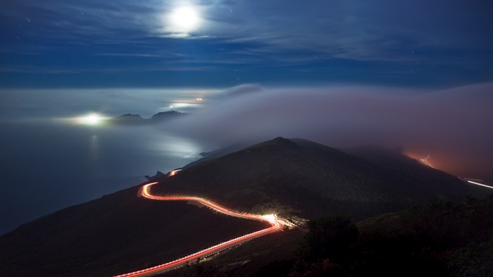 Night road with light trails along the coast under the moon