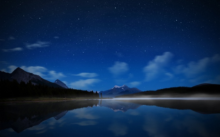 Starry night sky over a misty lake and mountains