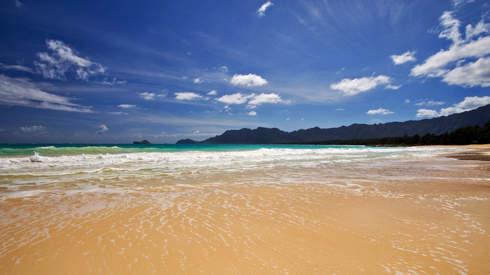 Beach with waves and mountains under a blue sky