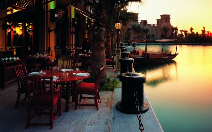 Outdoor restaurant seating by a canal at sunset