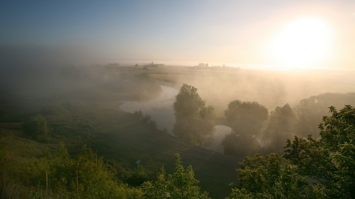 Misty river landscape at sunrise with sun and trees