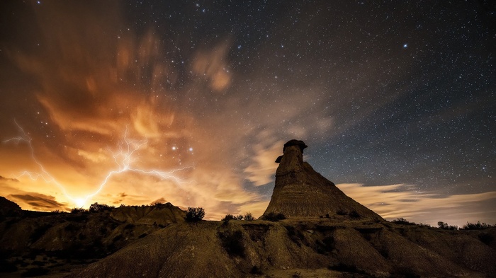 Lightning strikes over a rocky landscape under a starry sky