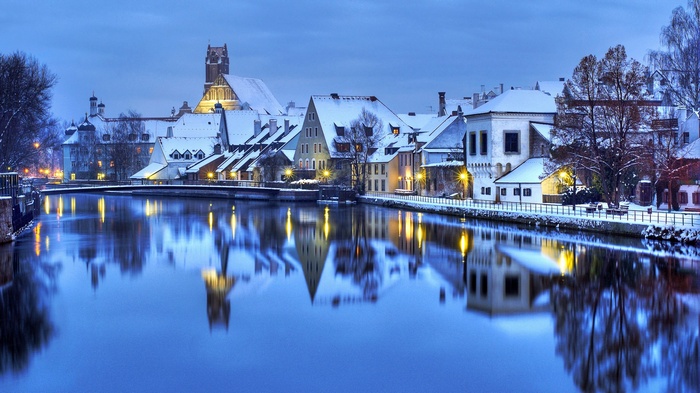 Winter cityscape with snow-covered buildings and river reflections
