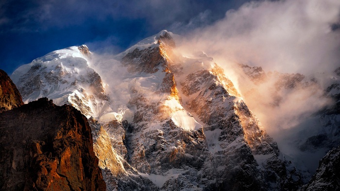 Snowy mountain peak illuminated by sunlight through clouds