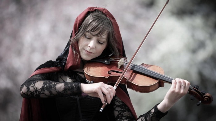 Lindsey Stirling plays the violin wearing a red cloak