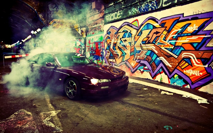 Maroon car doing a burnout in front of graffiti