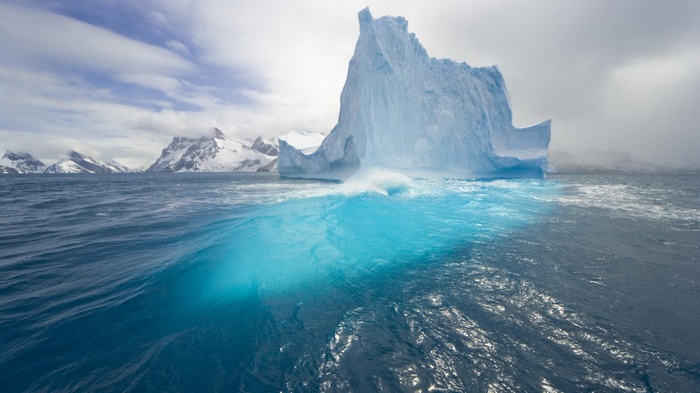 Iceberg in the Arctic sea with snow-capped mountains