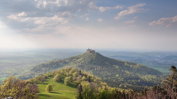 Burg Hohenzollern castle on a green hill with clouds