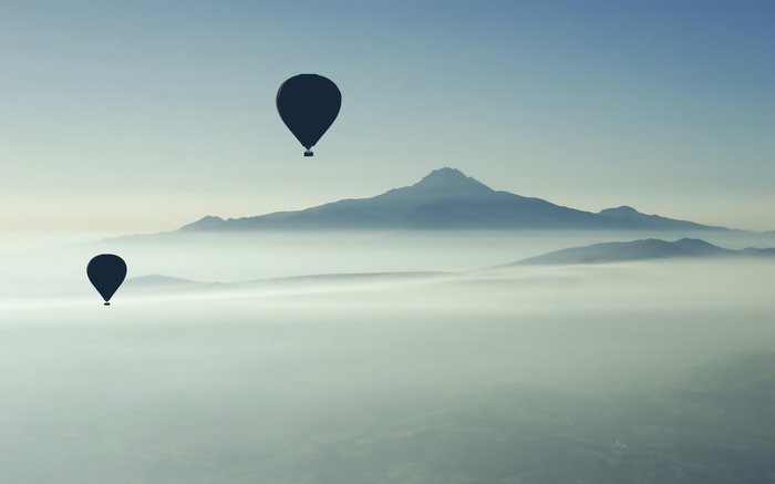 Two hot air balloons float over misty mountains