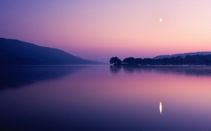 Purple lake and mountains at dusk with crescent moon