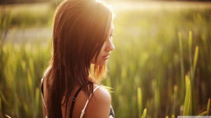 Woman with long brown hair in a field at sunset